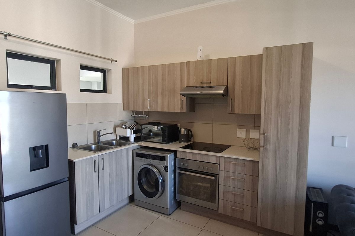 Compact kitchen featuring modern wood-look cabinetry, integrated appliances, tiled backsplash, and functional workspace, suitable for apartment living.