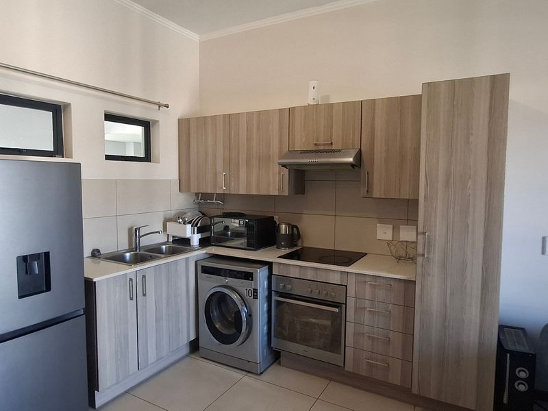 Compact kitchen featuring modern wood-look cabinetry, integrated appliances, tiled backsplash, and functional workspace, suitable for apartment living.