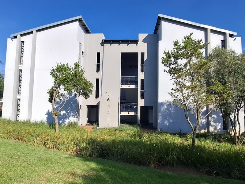 A view of the rear elevation of a modern apartment complex featuring balconies and well-maintained surrounding garden areas.