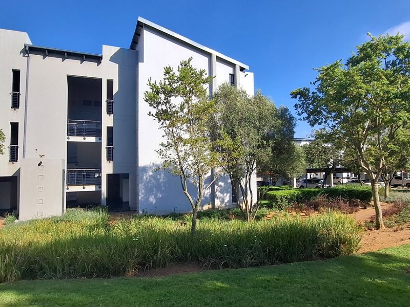 A view of the apartment building exterior featuring modern architecture, metal balcony railings, and well-maintained landscaped garden areas.