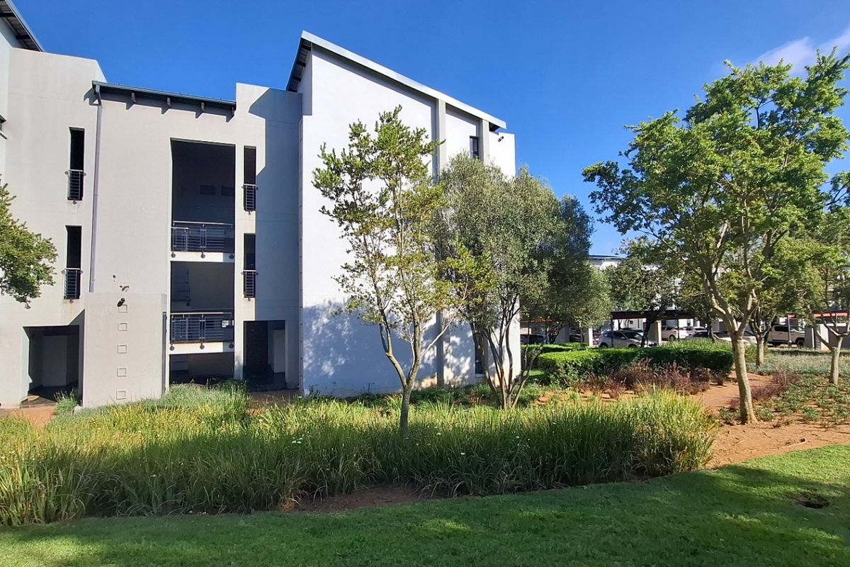 A view of the apartment building exterior featuring modern architecture, metal balcony railings, and well-maintained landscaped garden areas.