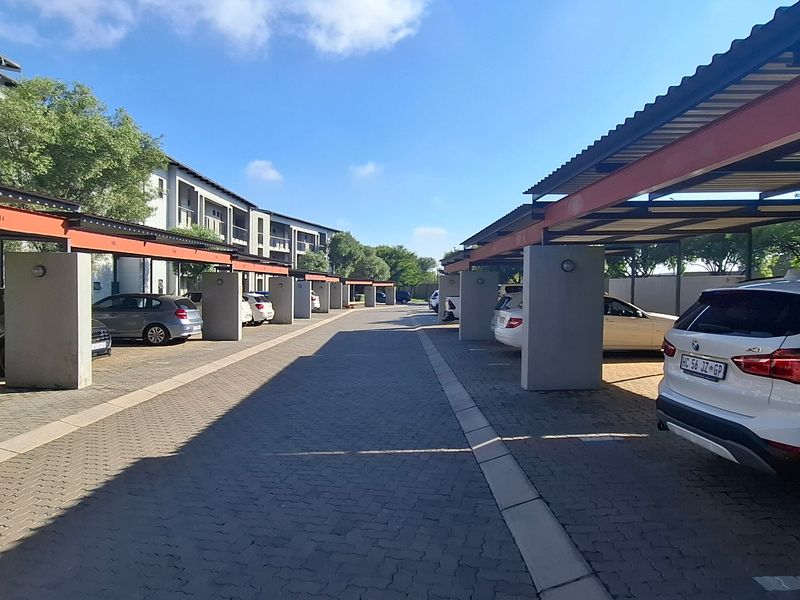 A well-maintained outdoor parking area featuring covered carports with concrete pillars and paved driveway surfaces within an apartment complex.
