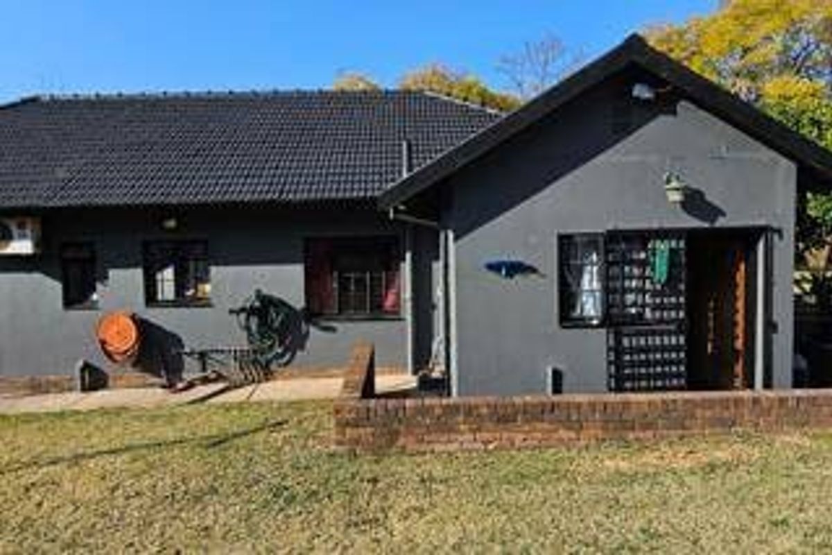 Rear view of the house featuring a dark tiled roof, grey painted exterior walls, and a low brick retaining wall bordering the garden area.
