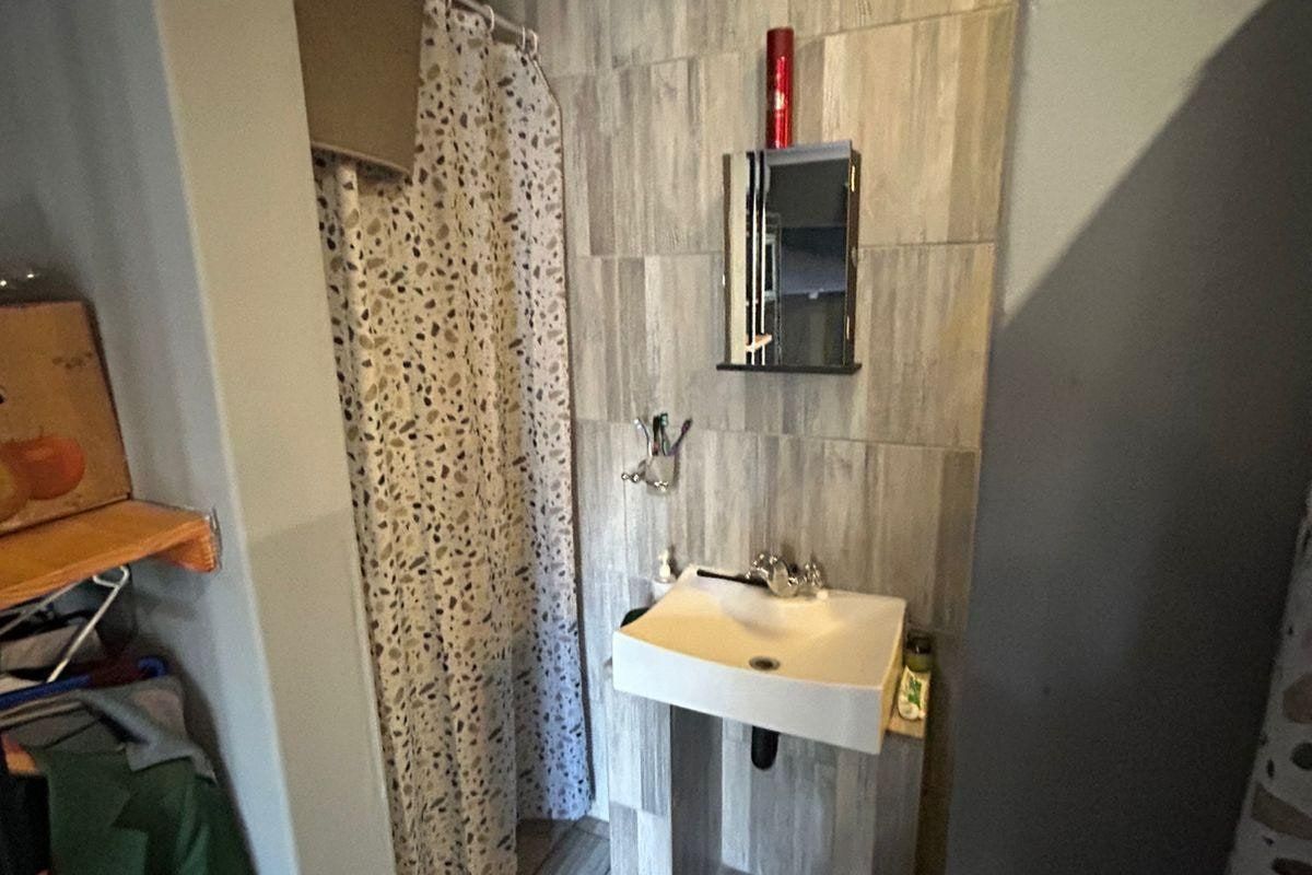 A compact bathroom featuring a wall-mounted basin, tiled wall finishes, and a shower area with a curtain.