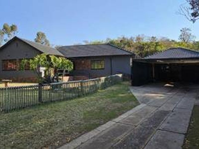 Front view of a residential house featuring a tiled roof, brick exterior, and a spacious carport with a paved driveway.