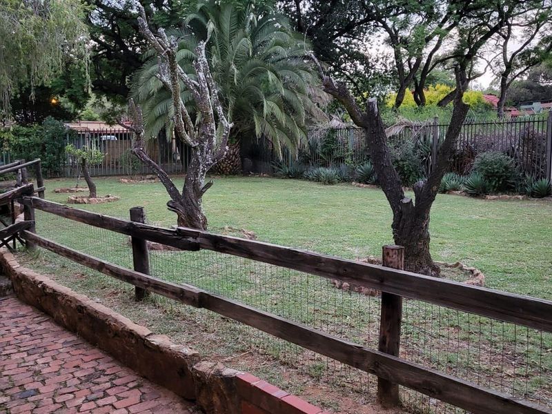 A spacious backyard featuring a brick-paved walkway, a rustic timber fence, and established trees set within a fenced perimeter.