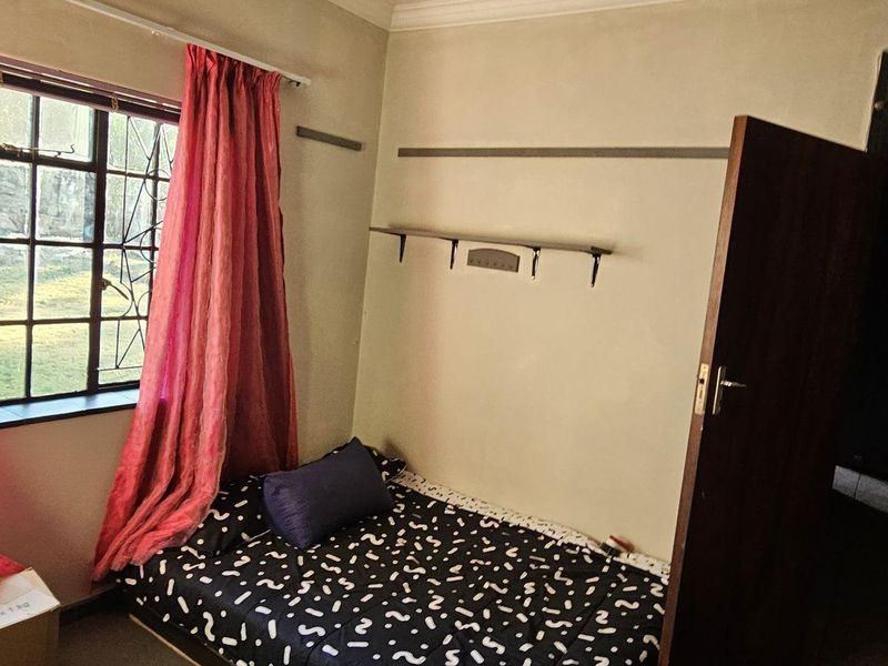 A compact bedroom featuring a ceiling fan, security bars on the window, and wall-mounted shelving.
