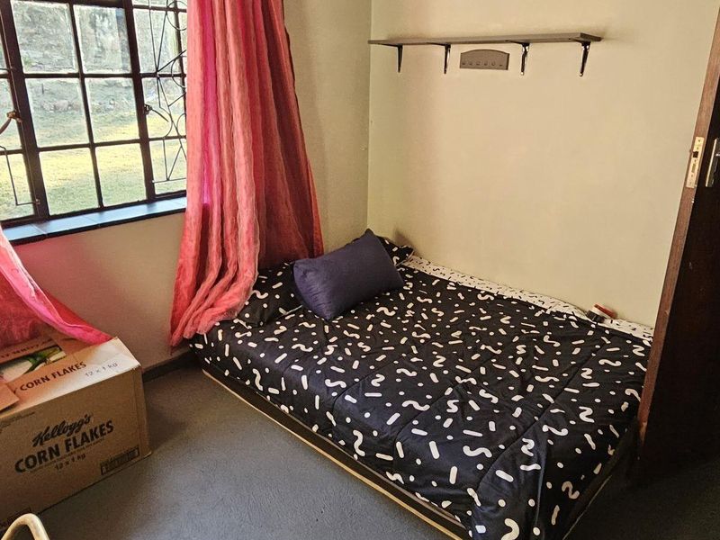 A compact bedroom featuring a steel-framed window, wall-mounted shelving, and neutral wall finishes, offering a functional space ready for cosmetic updates.