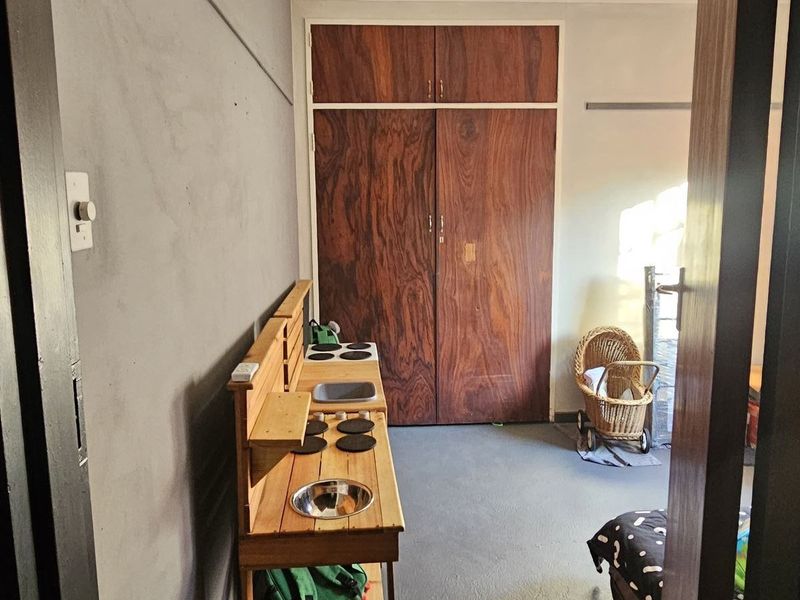 A bedroom featuring a built-in wooden wardrobe, ceiling fan, and coving, with neutral wall tones and painted flooring.