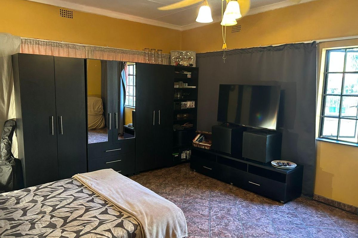 A bedroom featuring tiled flooring, a ceiling fan, and security burglar bars on the windows.