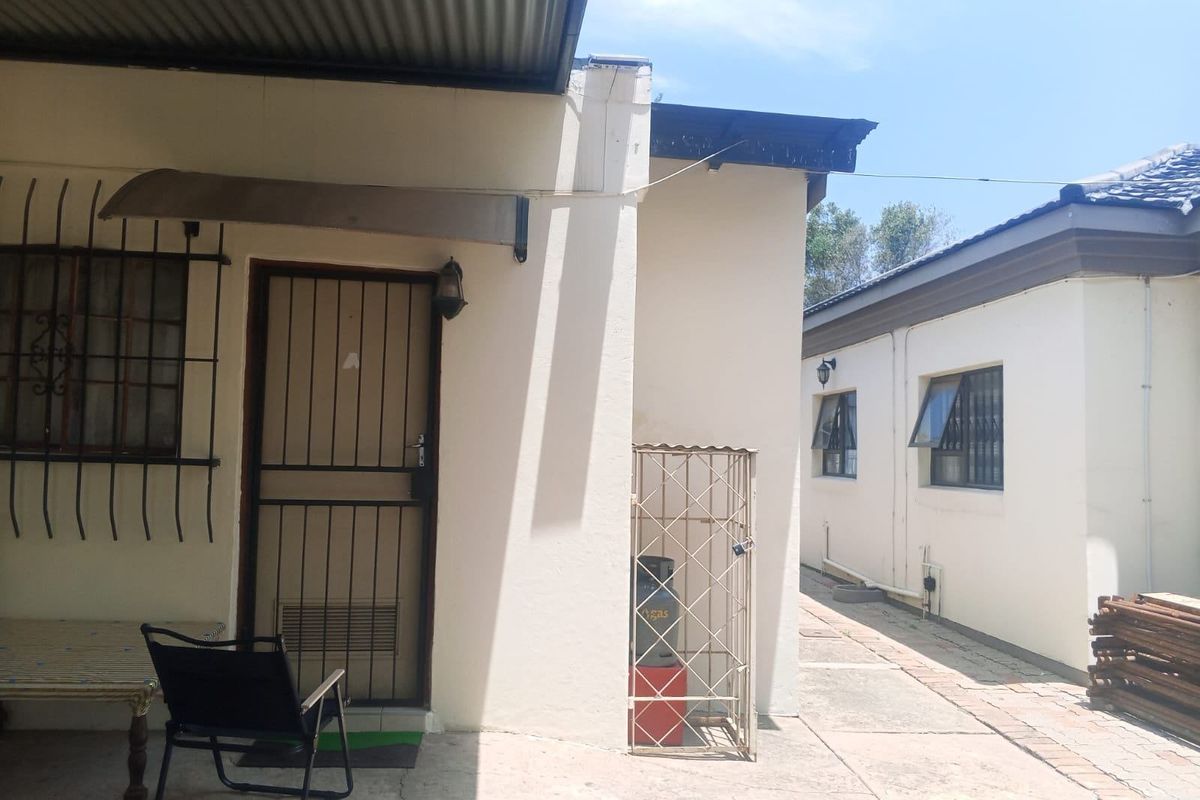 Rear exterior view showing a paved walkway, security gates, and metal roofing between two building structures.