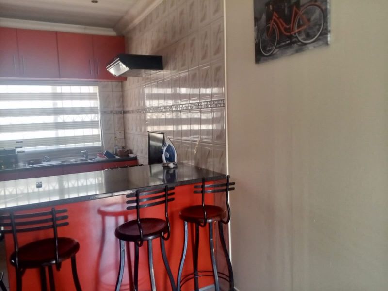 A functional kitchen featuring vibrant red cabinetry, a granite breakfast bar, and tiled splashbacks with an integrated extractor fan.