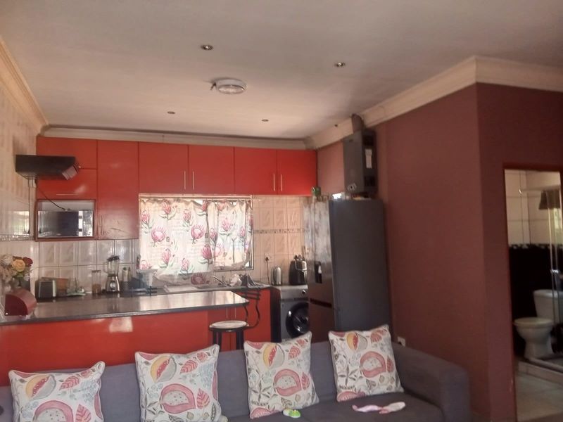 Open plan living area featuring a kitchen with orange cabinetry, tiled backsplash, and integrated extractor fan, adjacent to a living space.
