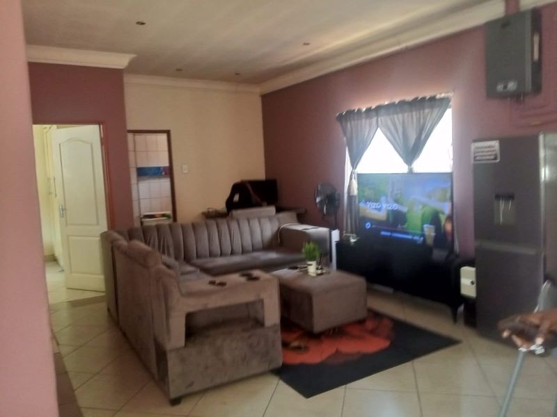 A living room featuring tiled flooring, recessed ceiling lighting, and coved cornicing, providing a functional space with direct access to adjacent rooms.