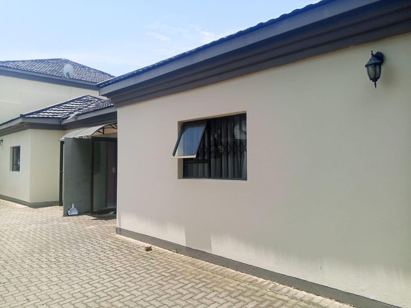 A view of the rear exterior facade featuring paved ground, security bars on the window, and an external wall light.