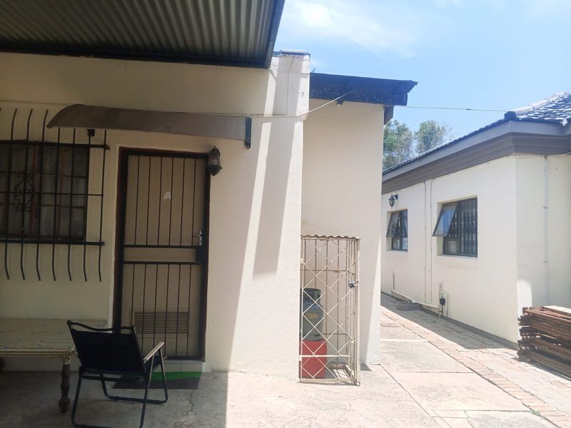 Rear exterior view showing a paved walkway, security gates, and metal roofing between two building structures.