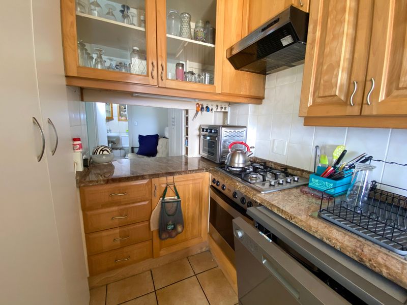 Compact kitchen featuring wooden cabinetry, granite countertops, gas hob, built-in oven, and extractor fan, with a convenient pass-through window to the adjacent living area.