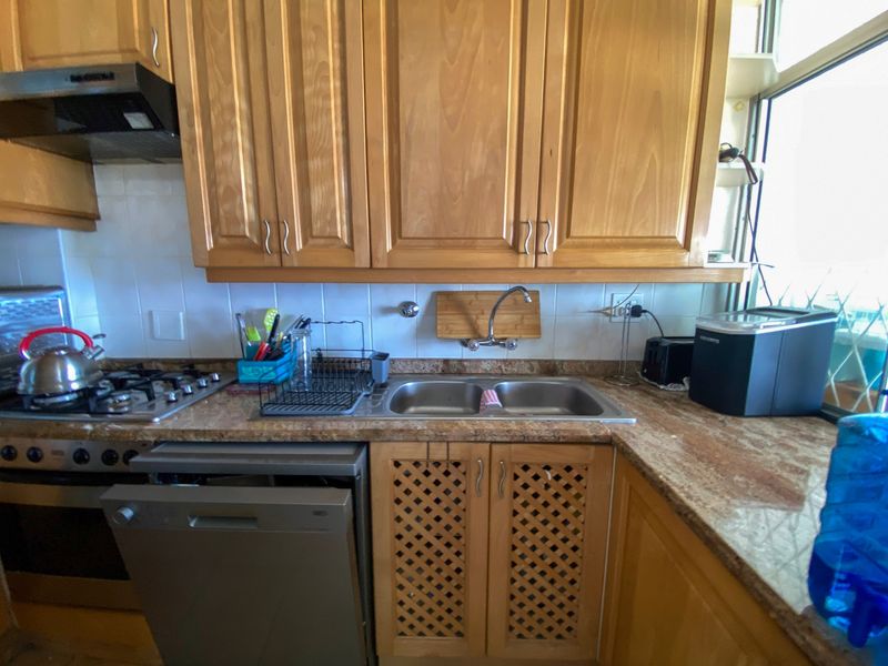 A functional kitchen featuring wooden cabinetry, stone countertops, a double bowl sink, gas hob, extractor fan, and an integrated dishwasher.