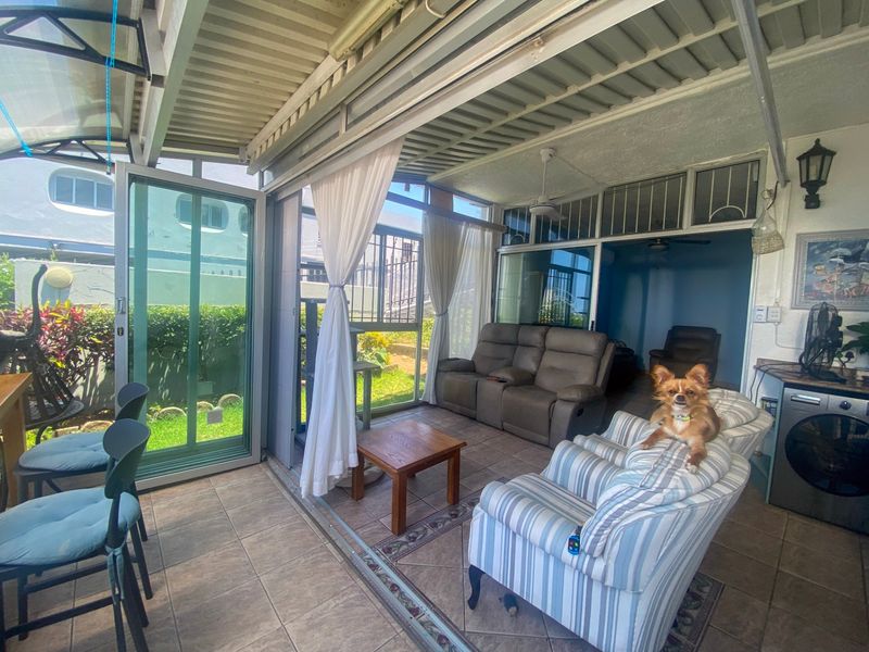 A covered patio area featuring tiled flooring, ceiling fan, and sliding glass doors, providing a seamless transition to the outdoor garden space.