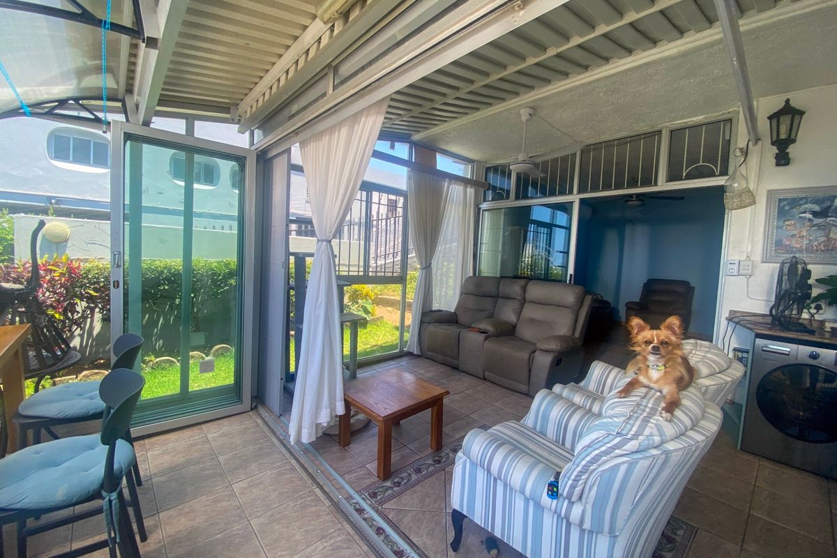 A covered patio area featuring tiled flooring, ceiling fan, and sliding glass doors, providing a seamless transition to the outdoor garden space.