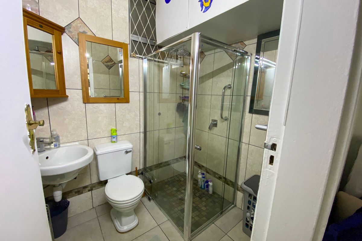 A functional bathroom featuring a glass shower enclosure, pedestal basin, and toilet with neutral wall and floor tiling.