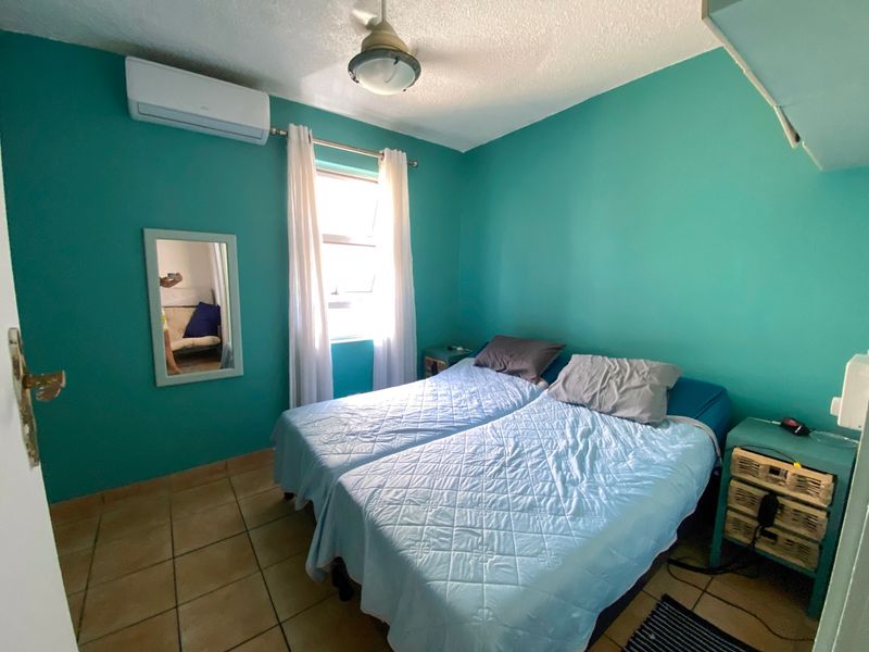 A bedroom featuring tiled flooring, a ceiling fan, and a wall-mounted split-system air conditioning unit.