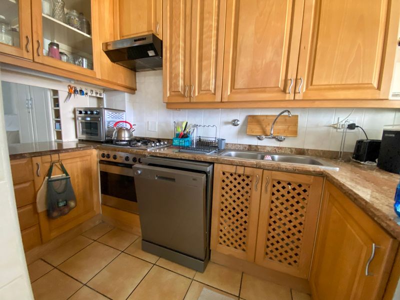 A functional kitchen featuring traditional wooden cabinetry, laminate countertops, a built-in oven with gas hob, and tiled flooring.