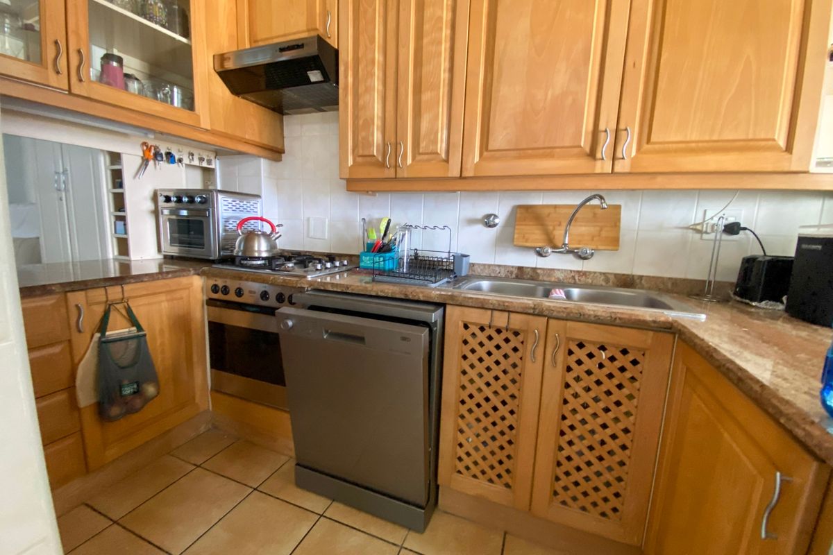 A functional kitchen featuring traditional wooden cabinetry, laminate countertops, a built-in oven with gas hob, and tiled flooring.