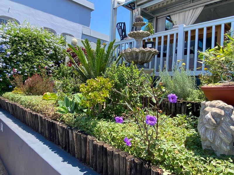 A well-maintained garden bed featuring a stone fountain, timber log edging, and established greenery, situated in front of a raised balcony area.