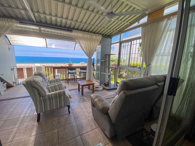A covered patio area featuring tiled flooring, a ceiling fan, and expansive ocean views, providing a seamless transition to outdoor living.