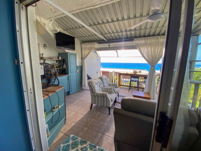 Covered patio area featuring tiled flooring, built-in cabinetry with stone countertops, and a ceiling fan, offering direct access to an outdoor balcony with ocean views.