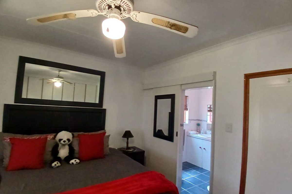 A bedroom featuring a ceiling fan and an adjoining en-suite bathroom, with neutral walls and a sliding door entrance.