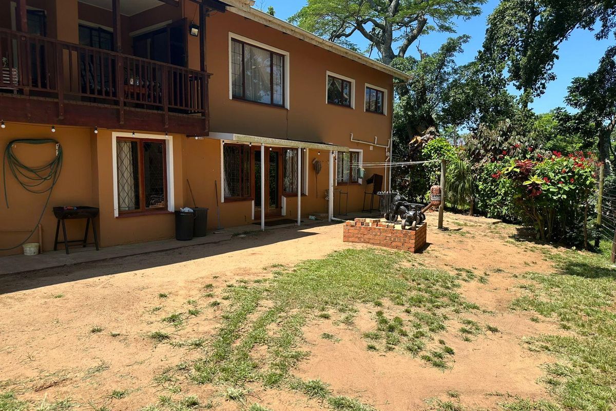 Rear view of the townhouse featuring a timber balcony, covered patio area, and a brick fire pit set within a large garden space.