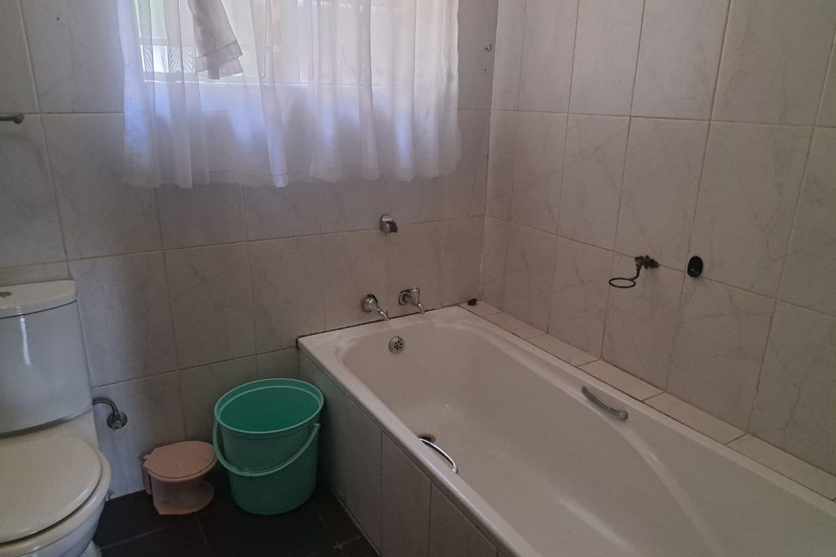 A functional bathroom featuring a built-in bathtub, tiled walls, and a standard toilet, requiring some minor maintenance and fixture updates.