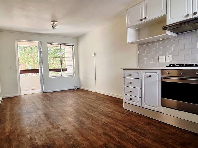 Open-plan kitchen and living area featuring modern laminate flooring, white cabinetry, subway tile backsplash, and direct access to a balcony.