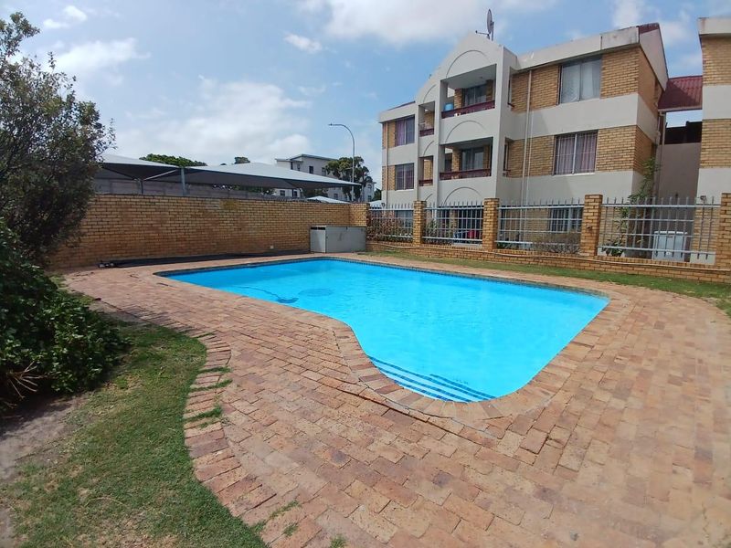 Communal swimming pool area featuring brick paving, perimeter walling, and metal security fencing, set within an apartment complex.