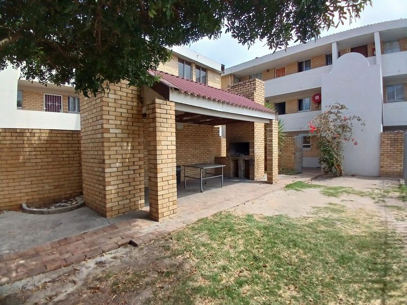 Communal outdoor area featuring a covered brick braai structure and paved patio space within an apartment complex setting.