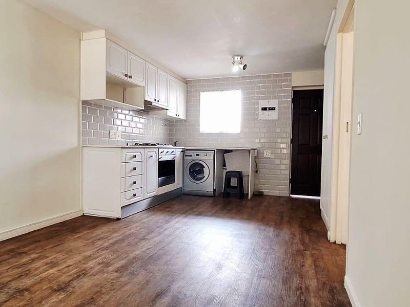 A functional kitchen featuring white cabinetry, subway tile backsplash, built-in oven, gas hob, and integrated laundry plumbing with durable laminate flooring.