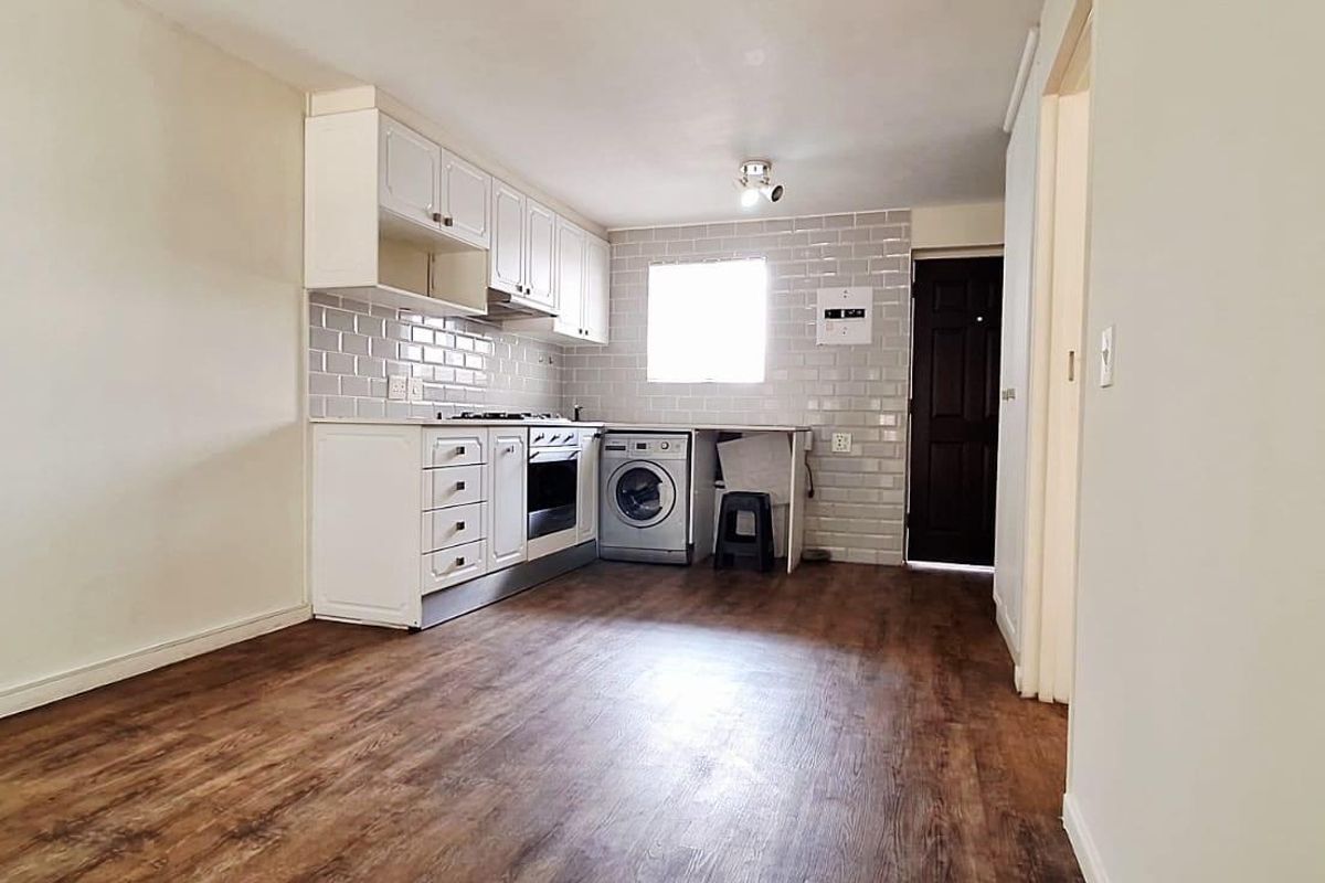 A functional kitchen featuring white cabinetry, subway tile backsplash, built-in oven, gas hob, and integrated laundry plumbing with durable laminate flooring.