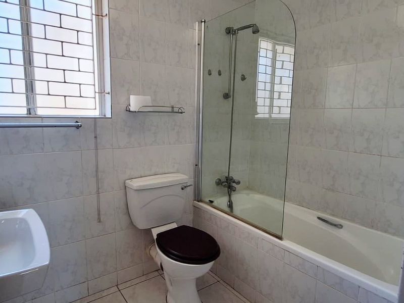 A functional bathroom featuring a bathtub with a glass shower screen, pedestal basin, and tiled walls, providing a clean and practical space.