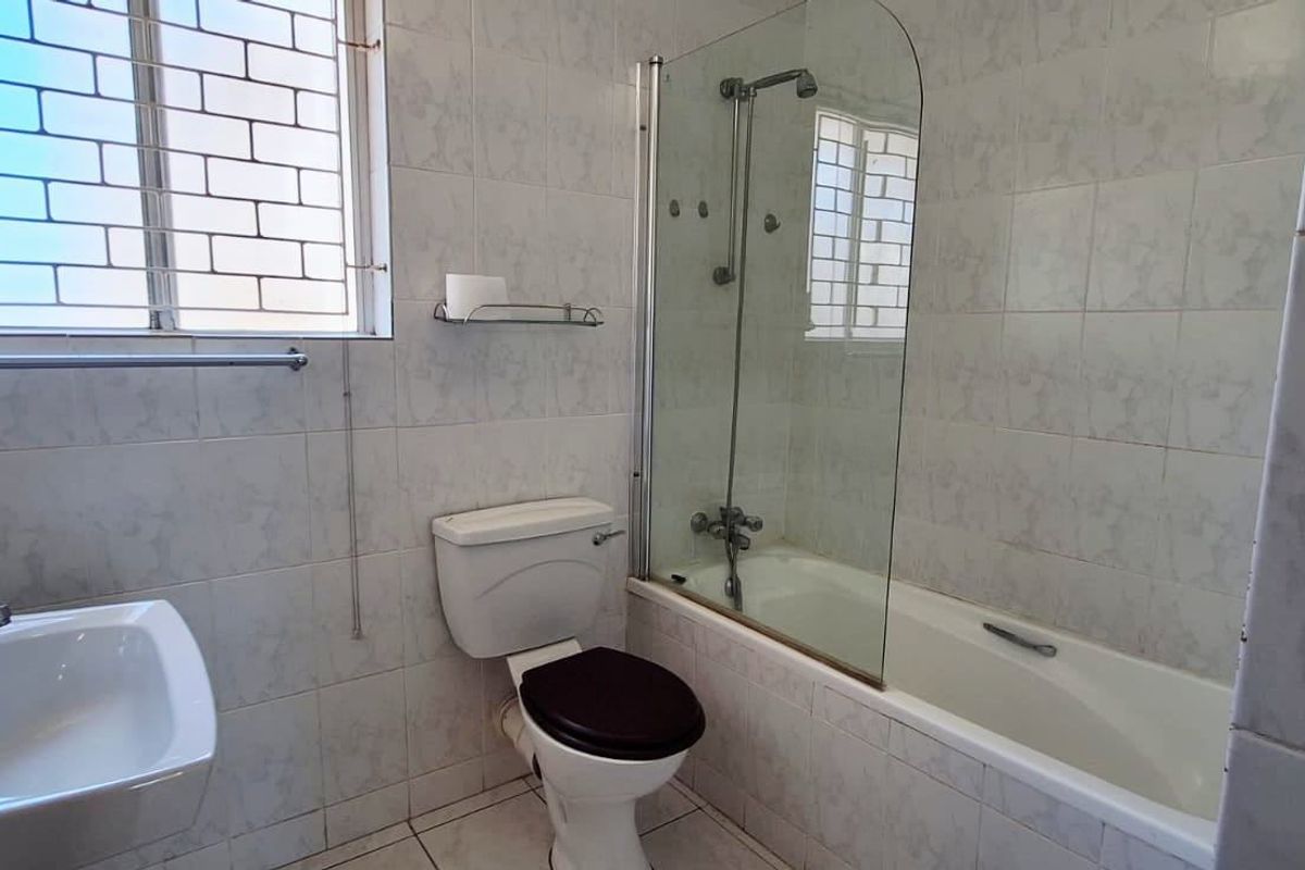 A functional bathroom featuring a bathtub with a glass shower screen, pedestal basin, and tiled walls, providing a clean and practical space.