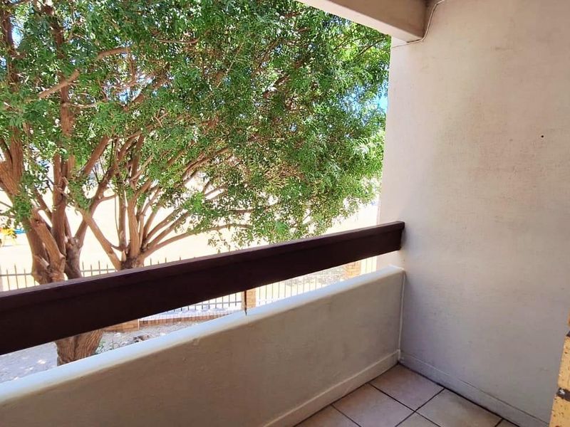 A compact balcony featuring tiled flooring, a timber handrail, and a brick pillar, offering a view of the surrounding trees.