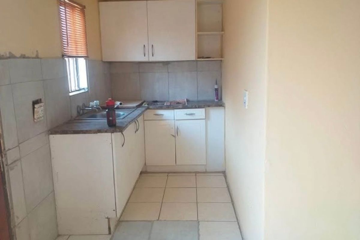 A compact kitchen featuring white cabinetry, laminate countertops, and tiled flooring. The space requires minor repairs and cosmetic updates to improve its overall condition.