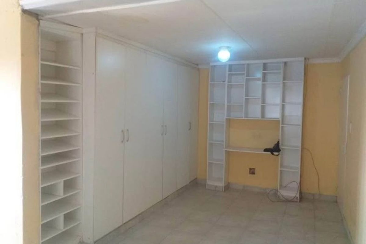 An empty bedroom featuring extensive built-in cabinetry, shelving, and a desk area with tiled flooring, requiring cosmetic updates to improve its overall condition.