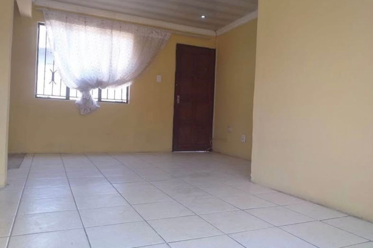 An empty living room featuring tiled flooring, a coved ceiling, and a window with security bars.