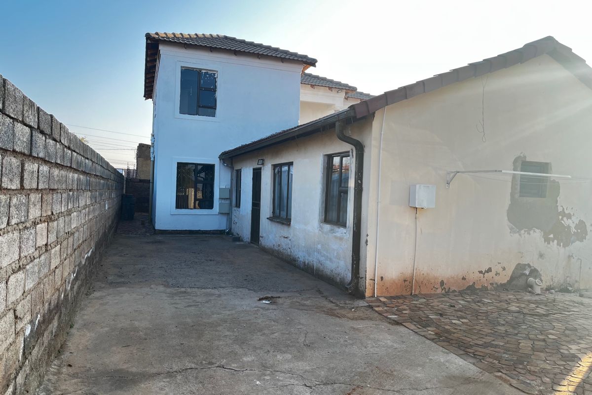 Rear exterior view of the property showing a concrete driveway, boundary wall, and the rear facade with visible wear to the exterior paintwork.