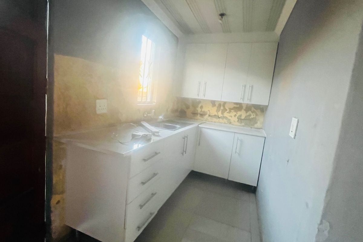 A compact kitchen area featuring white built-in cabinetry and a stainless steel sink, currently requiring wall finishing and cosmetic updates.