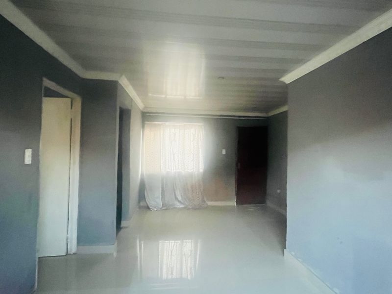 An empty living room featuring tiled flooring, a panelled ceiling with cornicing, and neutral grey walls.