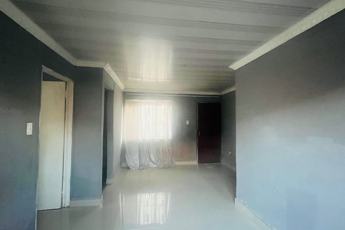 An empty living room featuring tiled flooring and neutral grey walls, offering a blank canvas for personalization.