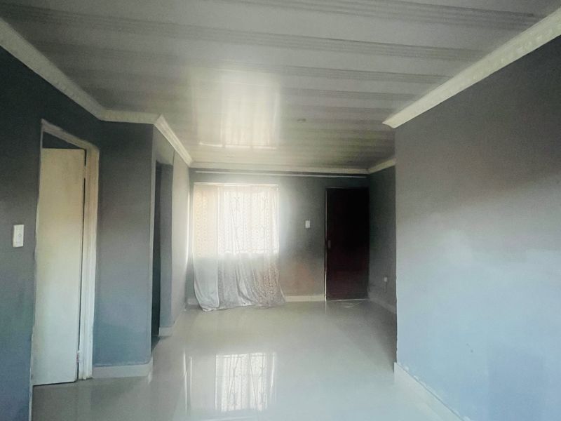 An empty living room featuring tiled flooring and neutral grey walls, offering a blank canvas for personalization.